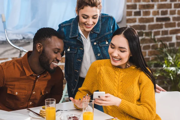 Smiling young multiethnic friends using smartphone together — Stock Photo