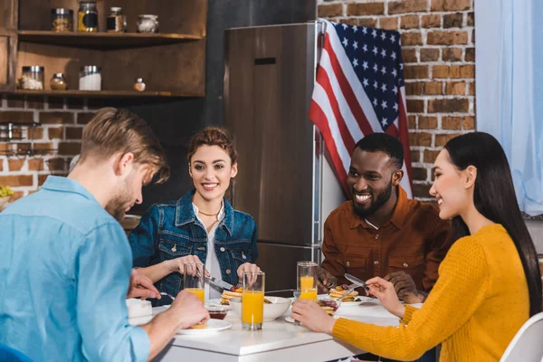 Happy young multiethnic friends eating pancakes and drinking juice together — Stock Photo