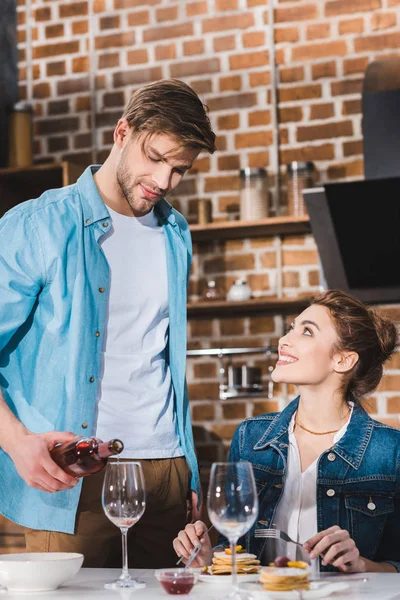 Bonito jovem derramando vinho para sorrir namorada em casa — Fotografia de Stock