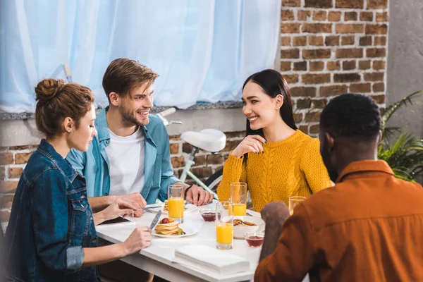 Happy young multiethnic friends eating breakfast and talking at table — Stock Photo