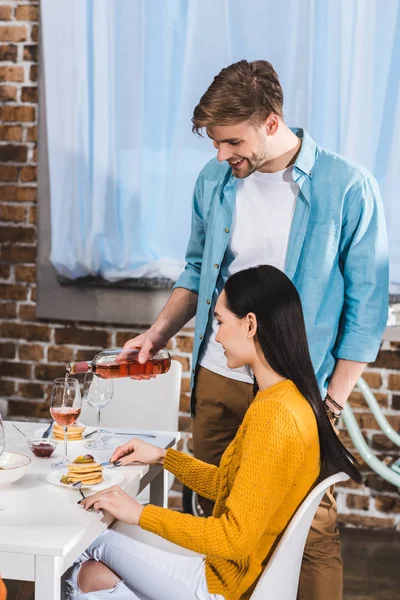 Souriant jeune homme versant du vin à belle petite amie à la maison — Photo de stock