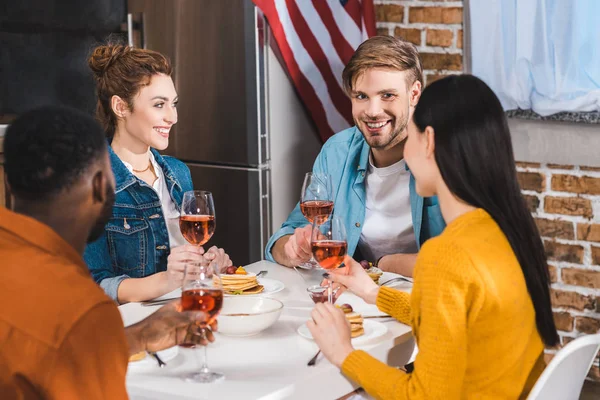 Felici giovani amici multietnici bere vino e parlare a tavola — Foto stock