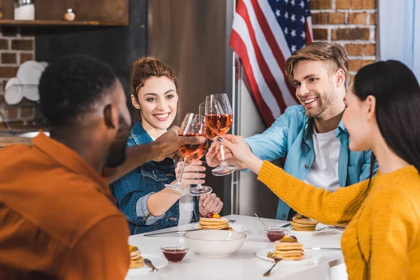 Happy young multiethnic friends clinking wine glasses above table — Stock Photo