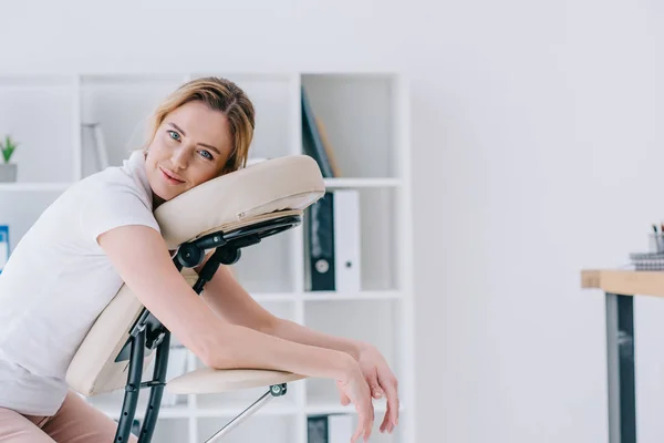 Feliz hermosa mujer sentado en silla de masaje en la oficina - foto de stock