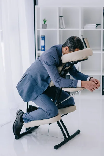 Homme d'affaires en costume assis dans une chaise de massage au bureau — Photo de stock