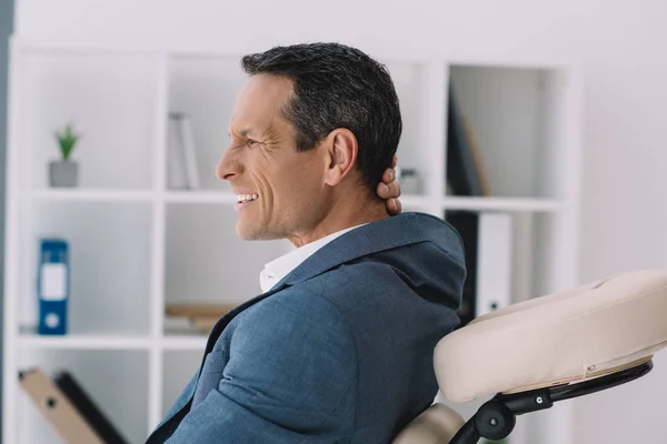 Empresário com dor nas costas dolorosa sentado na cadeira de massagem no escritório — Fotografia de Stock