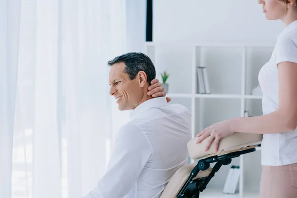 Businessman with pain in neck sitting in masseuse office — Stock Photo