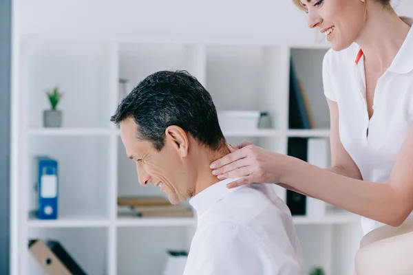 Vista lateral de masajista haciendo masaje de cuello sentado para el cliente en la oficina - foto de stock