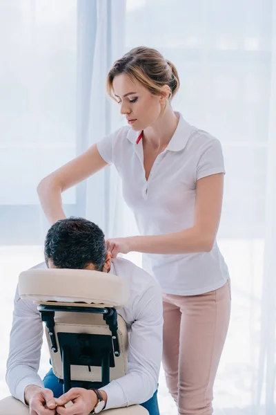 Massagista atraente fazendo massagem nos ombros no assento no escritório — Fotografia de Stock