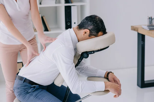 Massagista fazendo massagem nas costas no assento no escritório — Fotografia de Stock