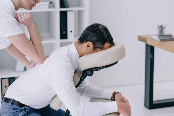 Masajista profesional haciendo masaje de espalda sentado para hombre de negocios en la oficina - foto de stock