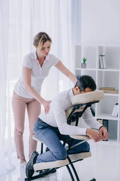 Masajista haciendo masaje de espalda para hombre de negocios en la oficina - foto de stock