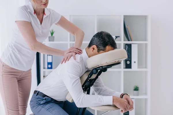 Hermosa masajista adulto haciendo masaje sentado para hombre de negocios — Stock Photo