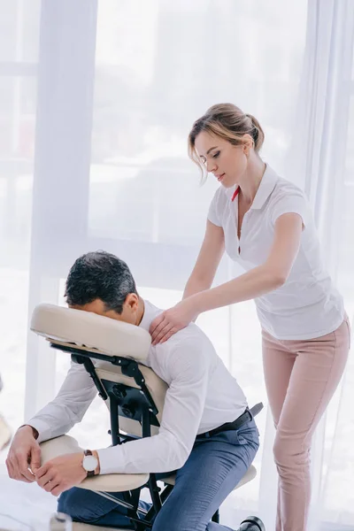 Hermosa masajista adulto haciendo masaje de oficina para hombre de negocios - foto de stock