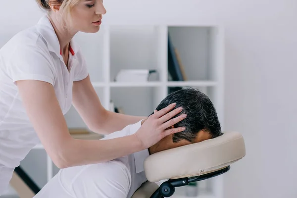 Vista lateral de masajista haciendo masaje en la cabeza para hombre de negocios - foto de stock