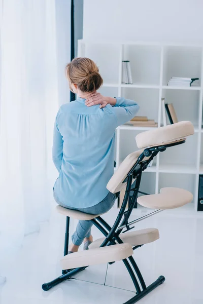 Vista trasera de mujer de negocios con dolor de cuello sentado en silla de masaje - foto de stock