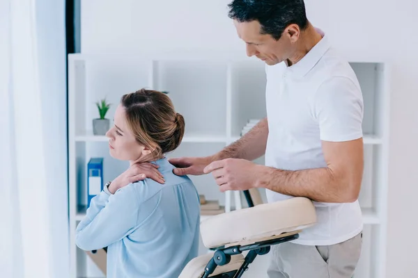 Masseur schaut Kundin mit Nackenschmerzen im Büro an — Stockfoto