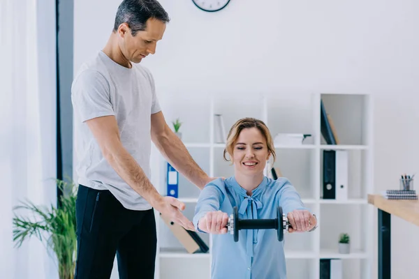 Attractive businesswoman doing squats with dumbbell with trainer at office — Stock Photo