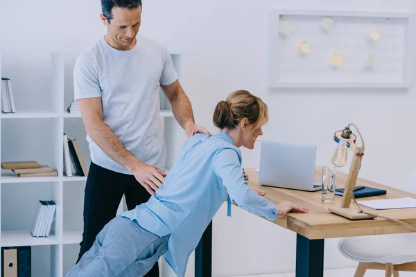 Businesswoman doing oush ups on workdesk with trainer at office — Stock Photo