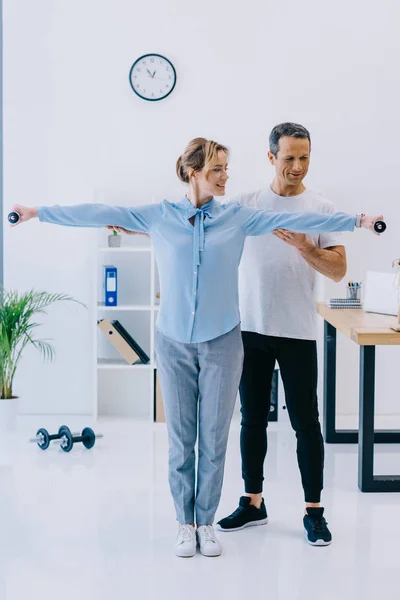 Bela mulher de negócios e seu personal trainer trabalhando com halteres no escritório — Fotografia de Stock