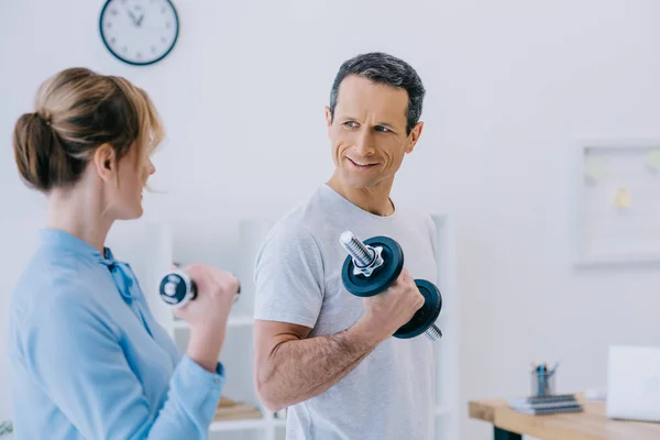 Businesswoman and her handsome mature personal trainer working out with dumbbells at office — Stock Photo