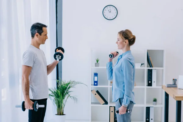 Side view of businesswoman and her personal trainer working out with dumbbells at office — Stock Photo