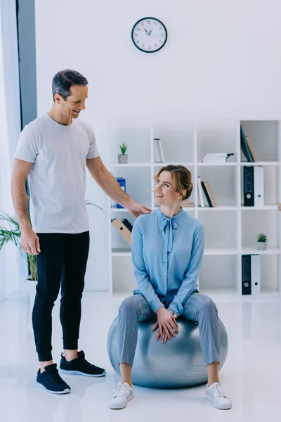 Mujer de negocios sentada en la pelota en forma y escuchando a su entrenador en la oficina - foto de stock
