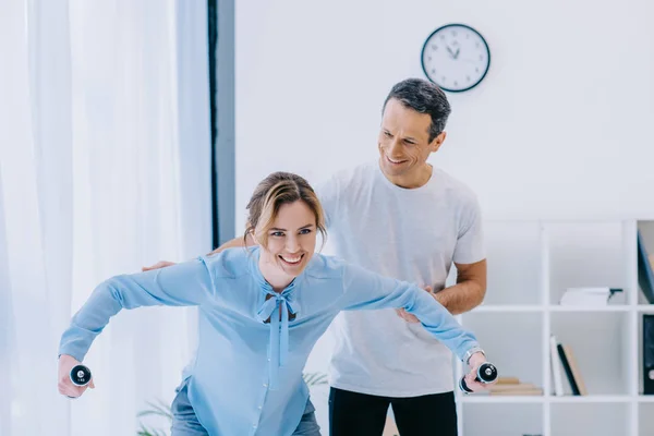 Mujer de negocios haciendo ejercicio con pesas con entrenador en la oficina - foto de stock