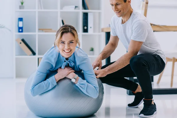 Mujer de negocios haciendo ejercicio en la bola en forma con entrenador en la oficina - foto de stock