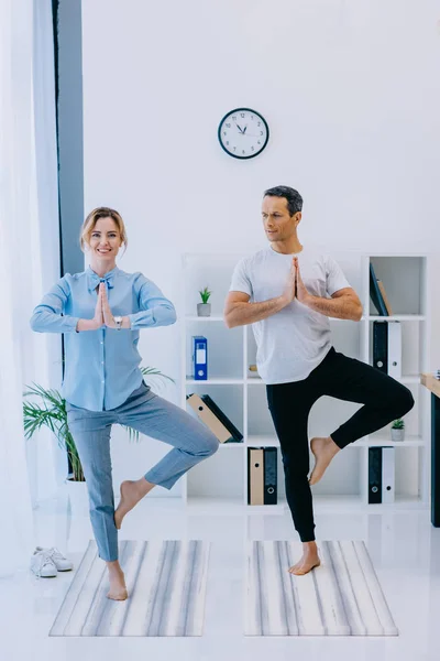 Mulher de negócios em forma com seu treinador praticando ioga em pose de árvore no escritório — Fotografia de Stock