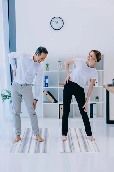 Mujer de negocios con su entrenador calentándose antes de practicar yoga en la oficina - foto de stock