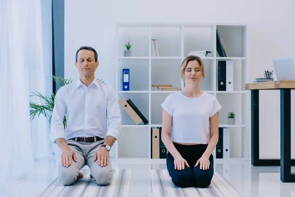 Hombre de negocios guapo con su entrenador meditando en esteras de yoga en la oficina - foto de stock