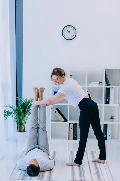 Geschäftsmann mit seinem Trainer, der Yoga im Büro praktiziert — Stockfoto