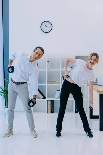 Maduro hombre de negocios con su entrenador personal femenino haciendo ejercicio con pesas en la oficina - foto de stock