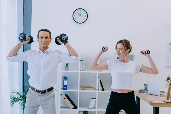 Businessman with his beautiful personal trainer working out with dumbbells at office — Stock Photo