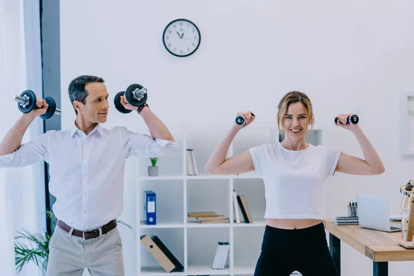 Happy mature businessman with his personal trainer working out with dumbbells at office — Stock Photo