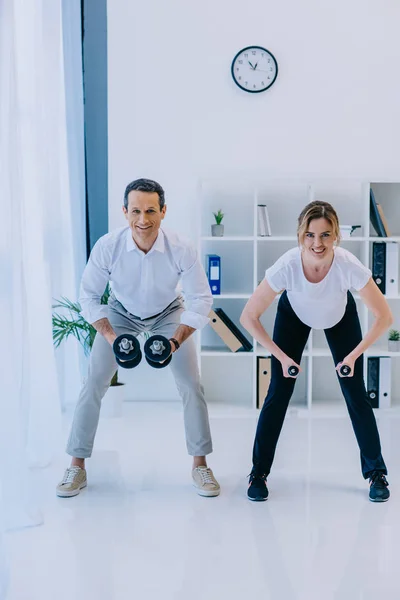 Guapo hombre de negocios con su entrenador personal femenino haciendo ejercicio con pesas en la oficina — Stock Photo