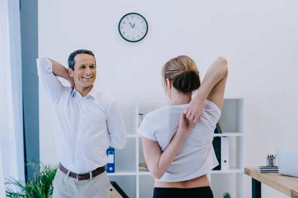 Handsome mature businessman stretching before workout with personal trainer — Stock Photo