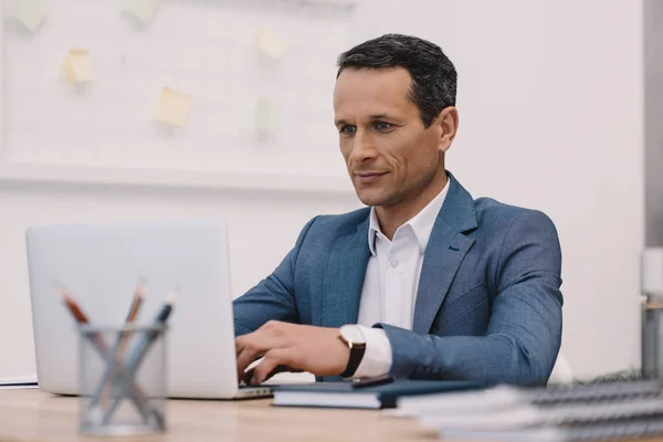Happy mature businessman using laptop at his workplace in office — Stock Photo