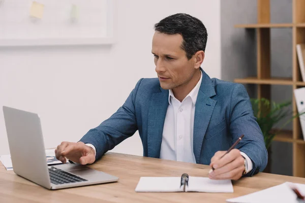 Businessman making notes while using laptop at workplace — Stock Photo