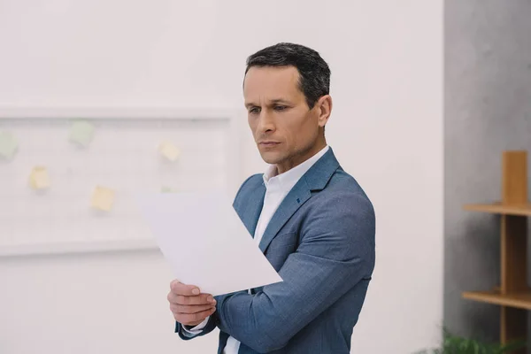 Зосереджений зрілий бізнесмен читає бізнес-папір в офісі — стокове фото