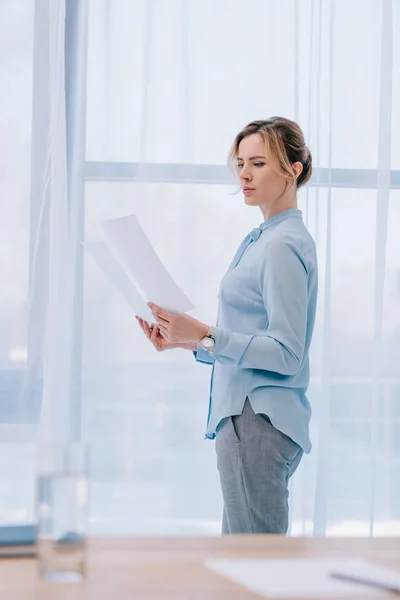 Приваблива бізнес-леді читає документи в офісі — стокове фото