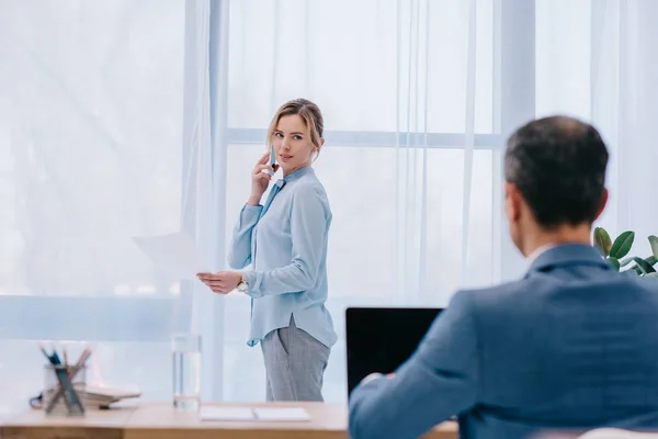 Businesswoman talking by phone at office while her colleague working with laptop on foreground — Stock Photo