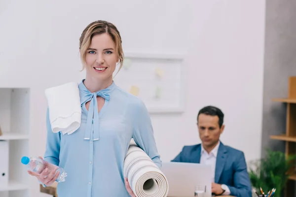 Empresária com equipamento de fitness em pé no escritório moderno, enquanto seu colega de trabalho com computador — Fotografia de Stock