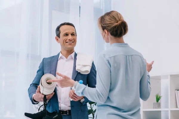 Handsome mature businessman with fitness equipment chatting with colleague before training at office — Stock Photo