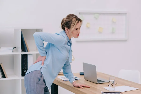 Перегруженная работой взрослая деловая женщина с болью в спине в офисе — стоковое фото