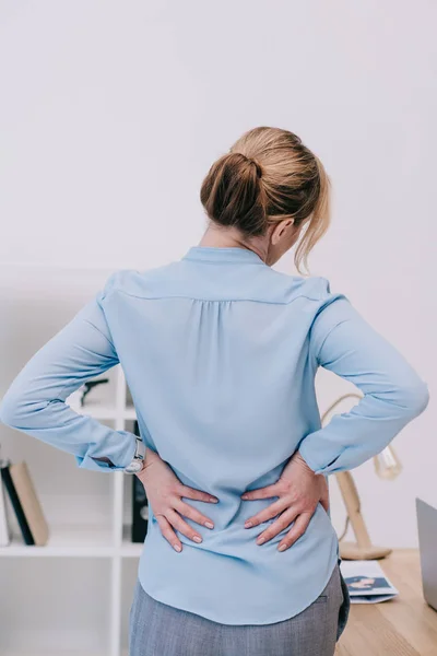 Vista posteriore della donna d'affari oberata di lavoro con mal di schiena appoggiata sul tavolo in ufficio — Foto stock