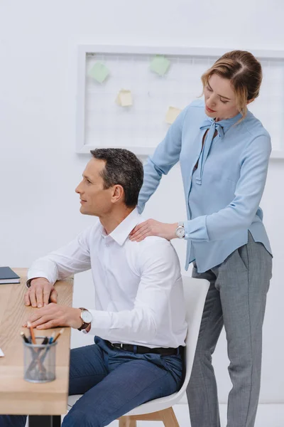 Homme d'affaires travaillant avec ordinateur portable sur le lieu de travail tandis que sa secrétaire faire un massage pour lui — Photo de stock