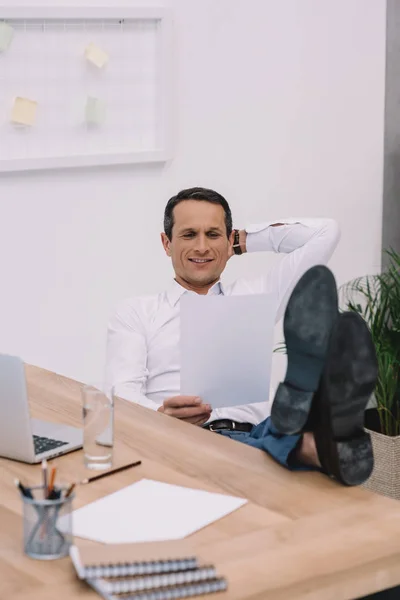 Handsome happy businessman relaxing and reading document at office — Stock Photo