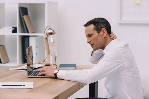 Middle aged businessman with neck pain working with laptop at office — Stock Photo